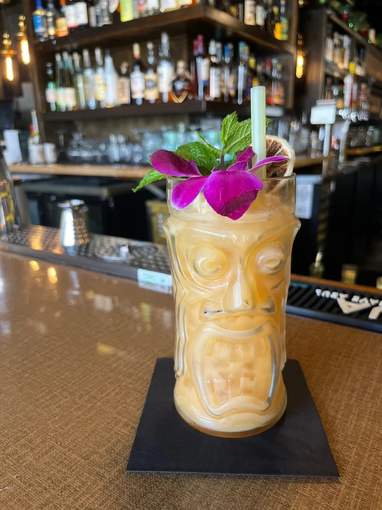 Amber tiki cocktail garnished with purple orchid, mint, and citrus wheel.