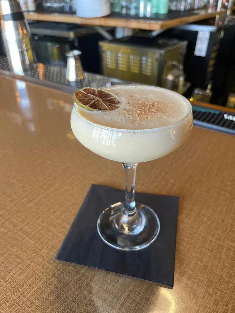 Creamy beige spiced cocktail with dried lime in a coupe glass.