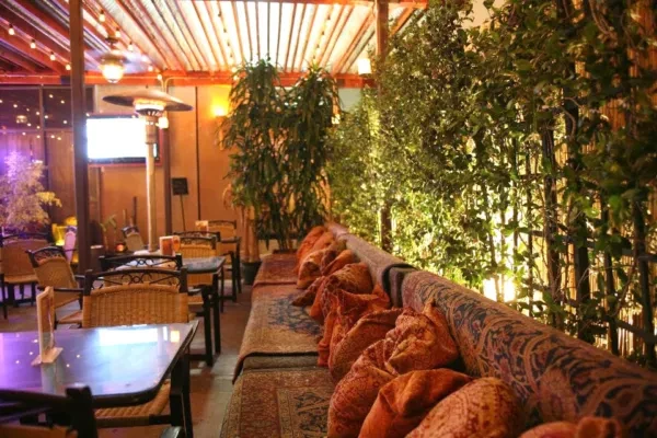 Empty outdoor restaurant lounge with banquettes, wicker chairs, and atmospheric lighting.