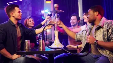 Five young adults toasting and smoking hookah in a dimly lit bar.
