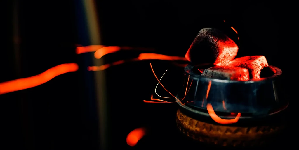 Close-up of glowing red shisha charcoal with sparks on dark background.