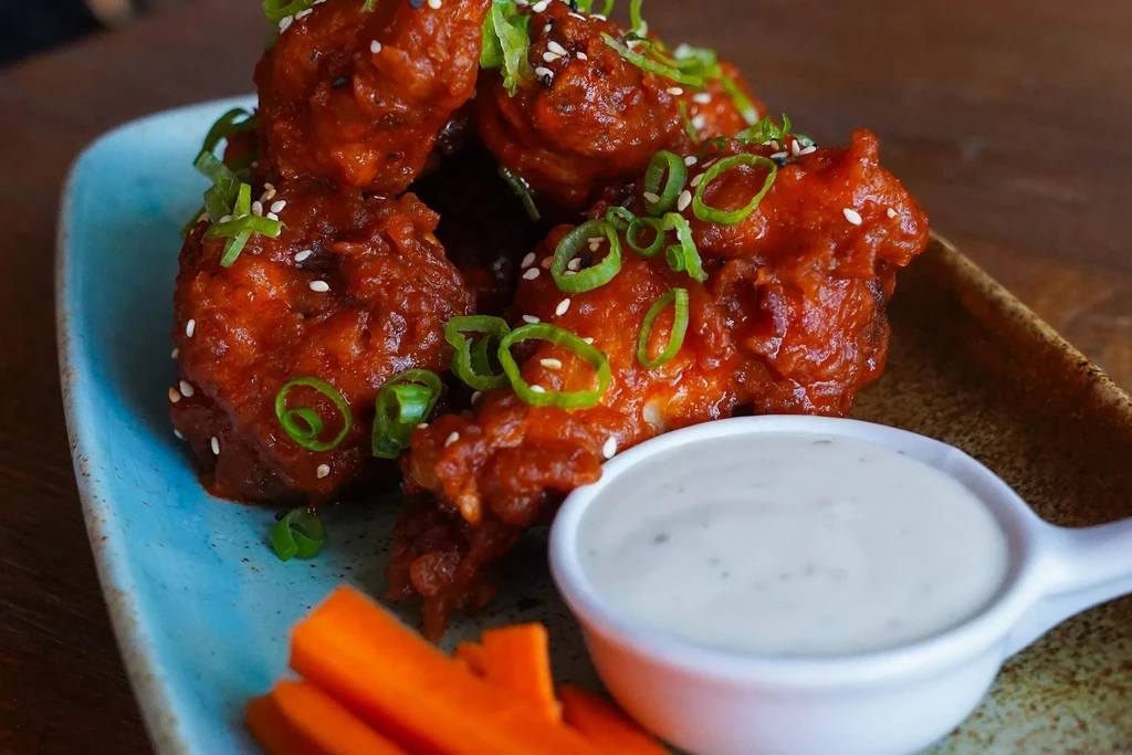 Boneless fried chicken in orange sauce, garnished with green onions and dip.