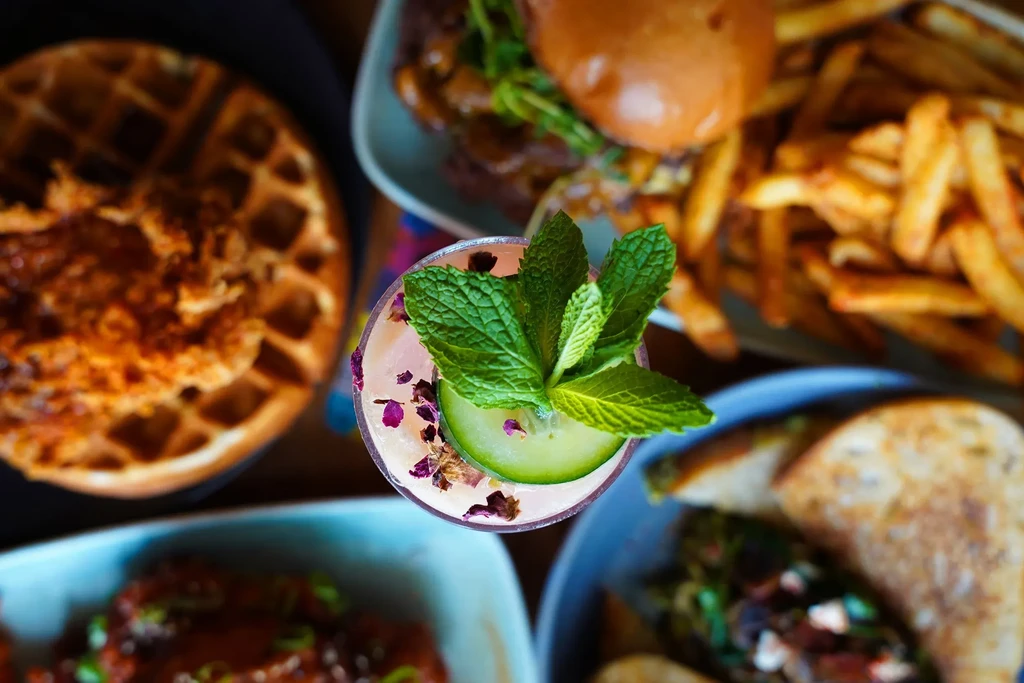 Overhead photo of a pink cocktail, burger, fries, and other restaurant dishes.