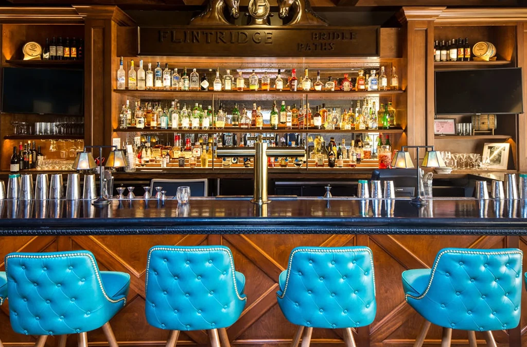 FLINTRIDGE BRIDLE PATHS bar with stocked shelves and turquoise stools.