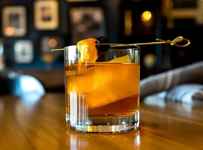 Old Fashioned in rocks glass with ice, orange peel, and cherry.