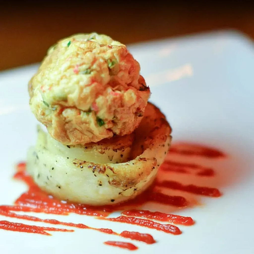 Golden fritter on grilled vegetable, red sauce on white plate.