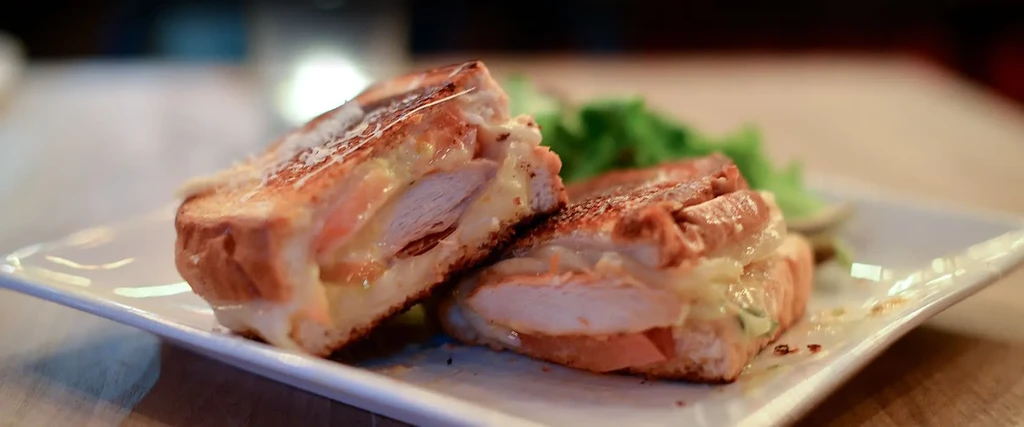 Grilled chicken and cheese sandwich with vegetables, cut in half.
