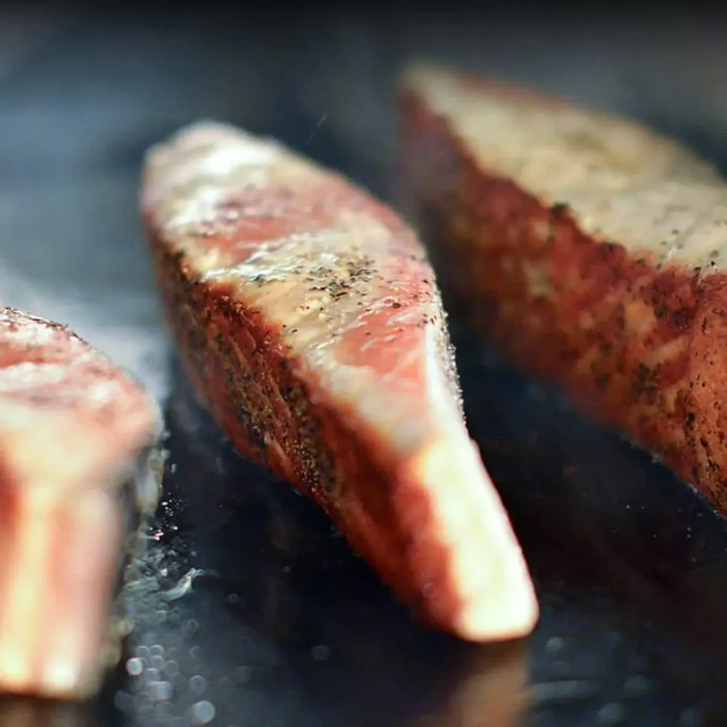 Three peppered steaks searing on a dark, hot griddle.