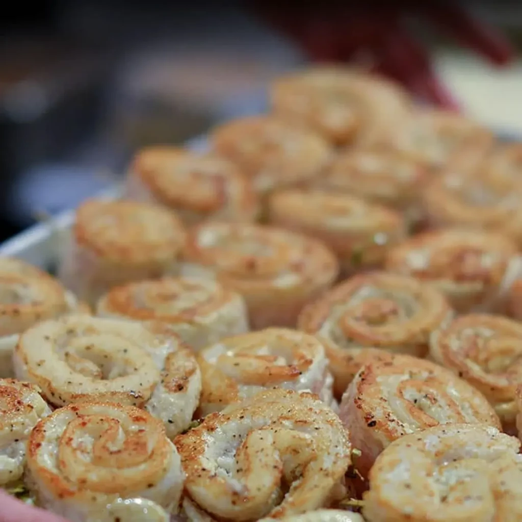 Golden-brown spiral food items, seasoned, on a tray with hands.