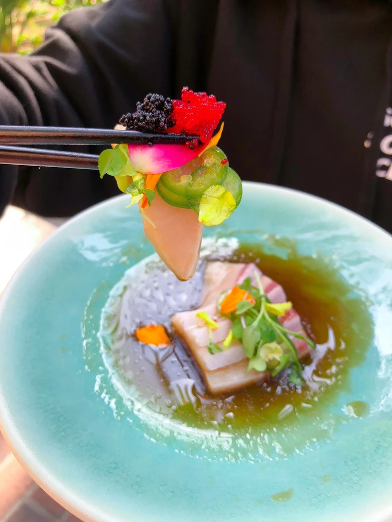 Japanese layered fish appetizer with pink slice and caviar, held by chopsticks.
