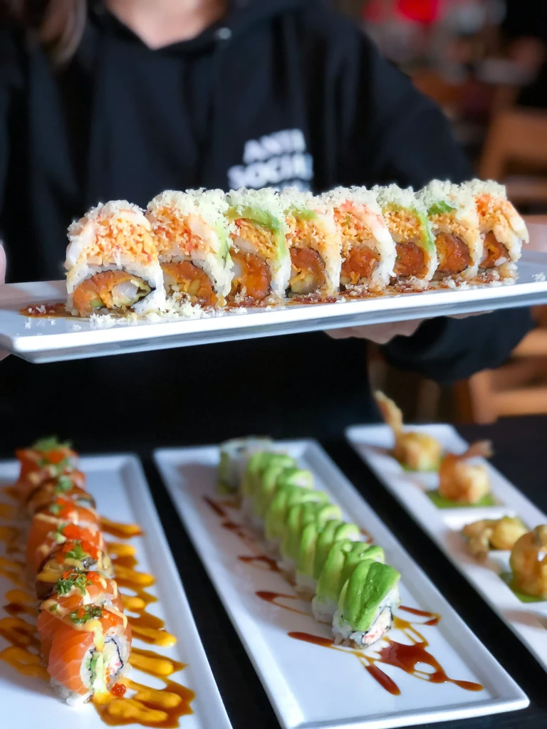 Close-up: Person holding crunchy sushi plate, more sushi plates behind.
