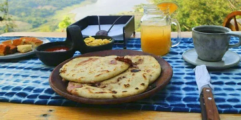 Outdoor dining table with food and drinks overlooks a scenic landscape.