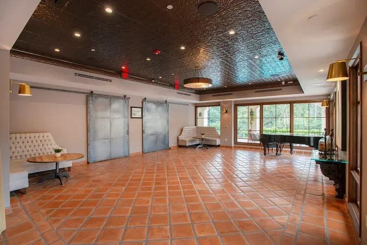 Terracotta floor, pressed tin ceiling, grand piano, and lush outdoor view.
