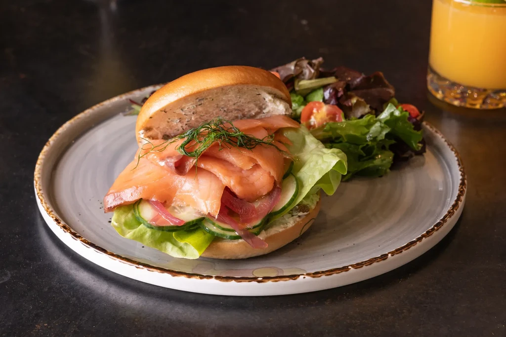 Open-faced salmon bagel sandwich with side salad and orange drink.