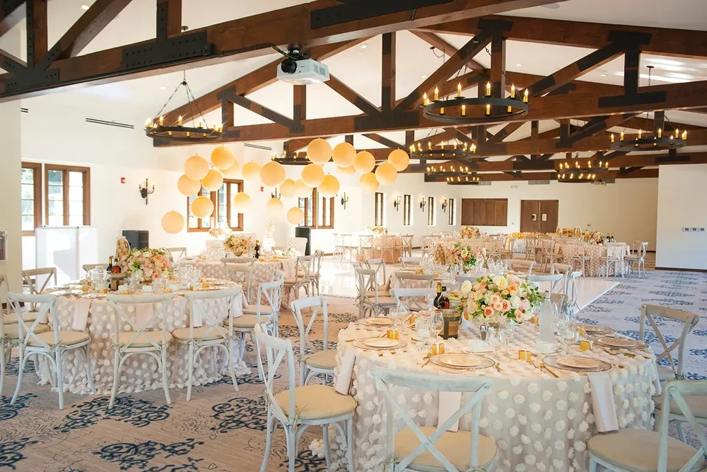 Elegant ballroom with floral dining tables, chandeliers, and festive balloons.
