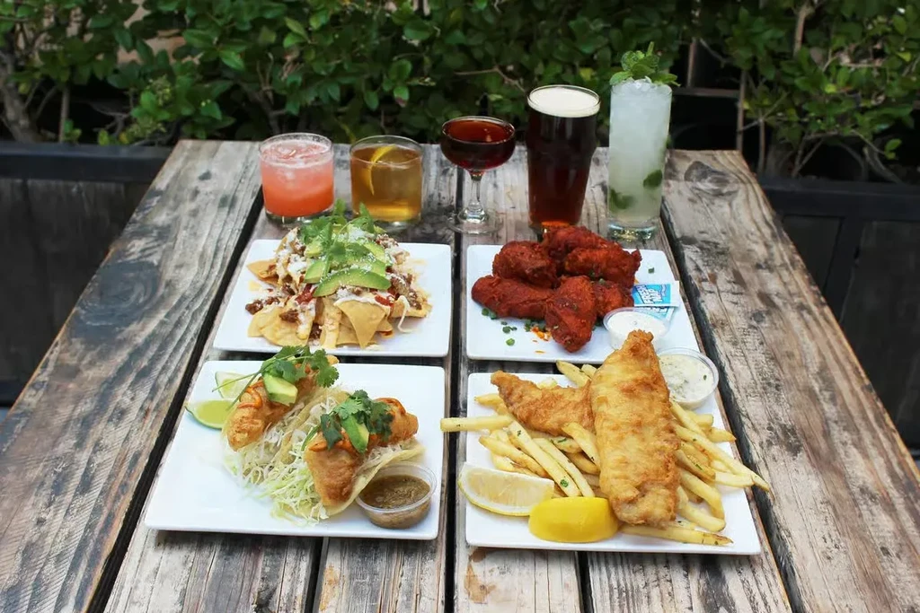 Outdoor table with nachos, wings, fish dishes, cocktails, and beer.