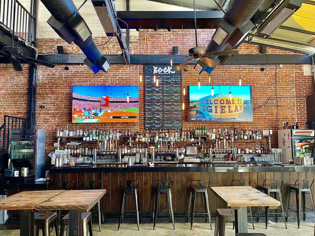 Well-stocked rustic industrial bar with sports and "WELCOME TO AGGIELAND".