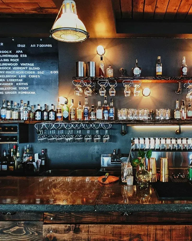 Warm, empty bar interior with liquor bottles, glasses, and bar tools.