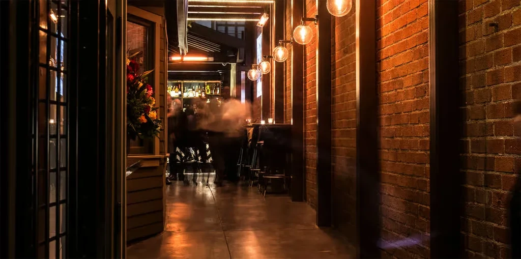 Dimly lit restaurant hallway with floral decor leading to a warm bar.
