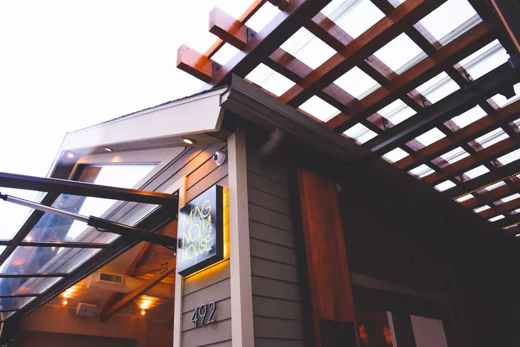Modern exterior of Magnolia House with illuminated sign, glass awning, pergola.