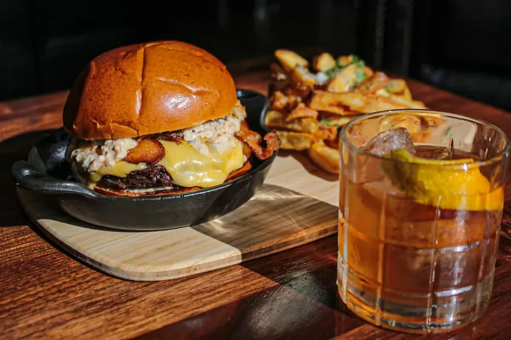 Burger, fries, and cocktail on a dark wooden table.