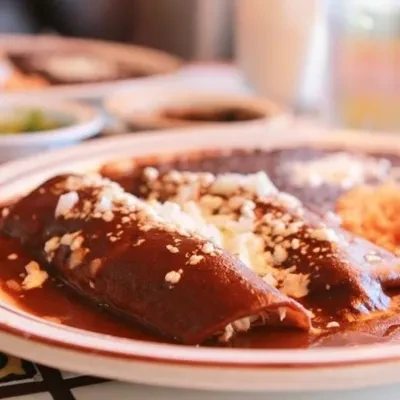 Close-up of two enchiladas with red sauce, crumbled cheese, and sides.