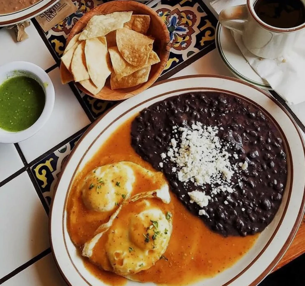 Overhead huevos rancheros, black beans, salsa, chips, and coffee.