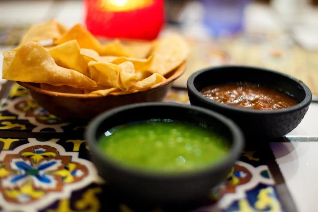 Tortilla chips, green and chunky red salsa on a patterned placemat.
