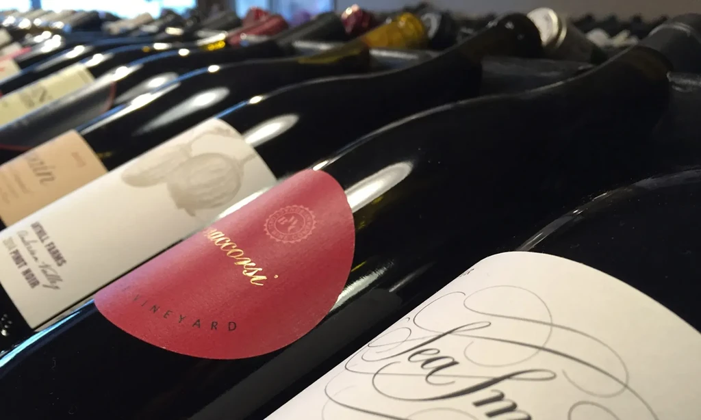 Horizontal dark wine bottles in rows, labels visible, including "Weill Farms".