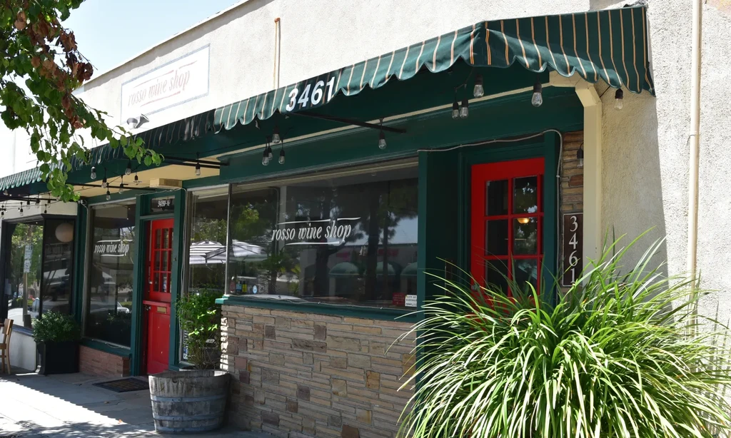 Rosso Wine Shop exterior with green awning, red door, and plants.