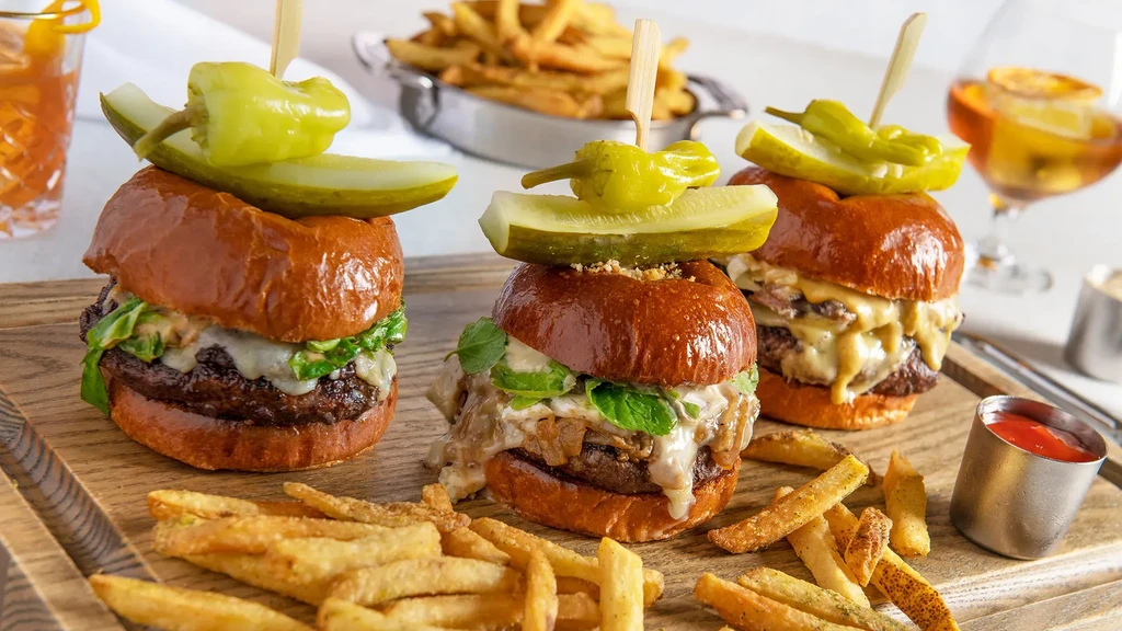 Three sliders, fries, pickles, and ketchup on a rustic wooden board.