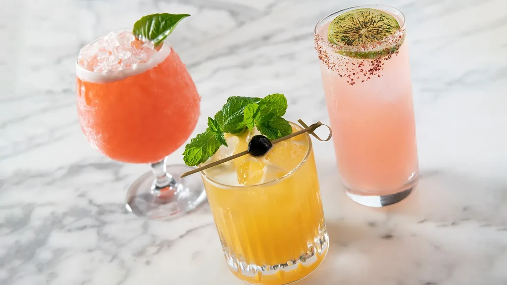 Vibrant coral, yellow, pink cocktails with garnishes on white marble.