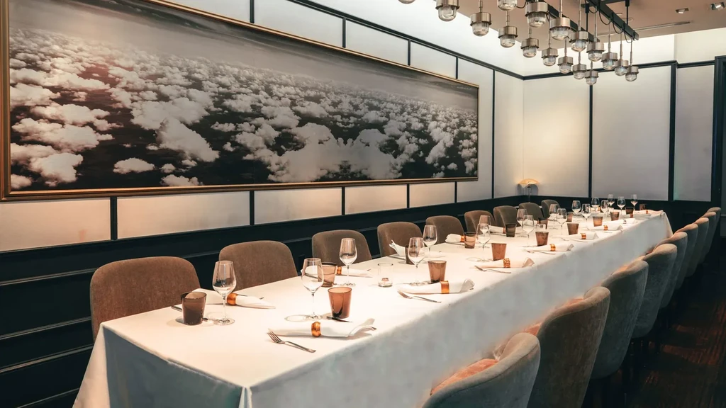 Modern restaurant interior with long set table and vast cloud artwork.