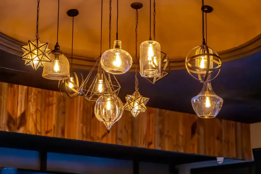 Diverse pendant lights with warm filament bulbs illuminate wood paneling.
