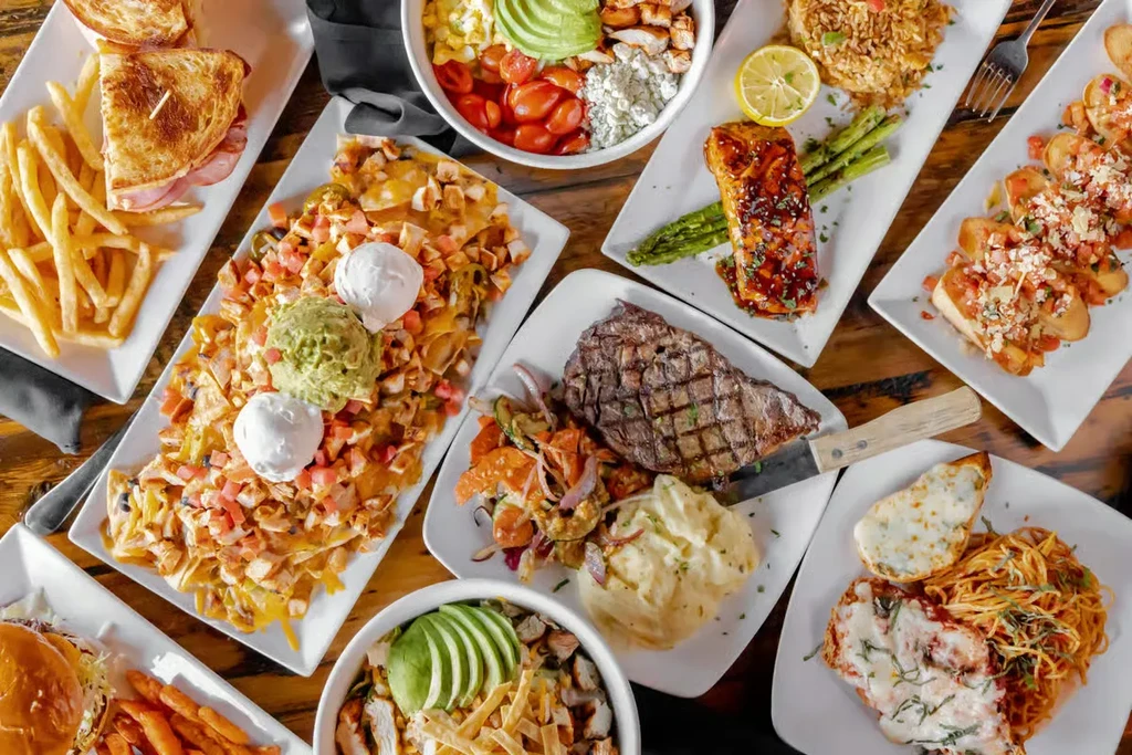 Overhead flat lay of a rustic table laden with diverse restaurant dishes.