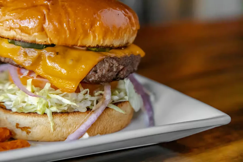 Close-up cheeseburger with melted cheddar, jalapeños, lettuce, and fries.