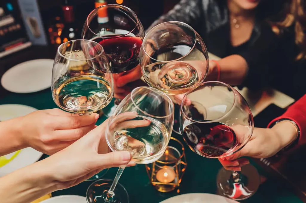 Overhead shot of five hands toasting with red and white wine glasses.