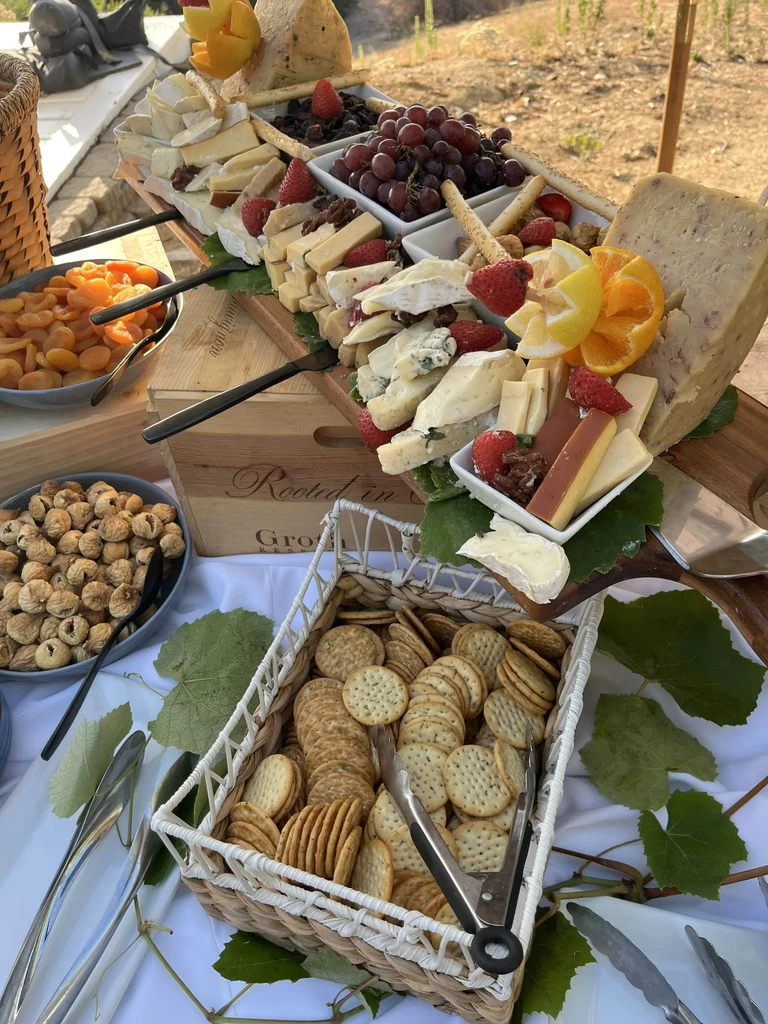 Abundant charcuterie board with cheeses, fruits, crackers, outdoor setting.