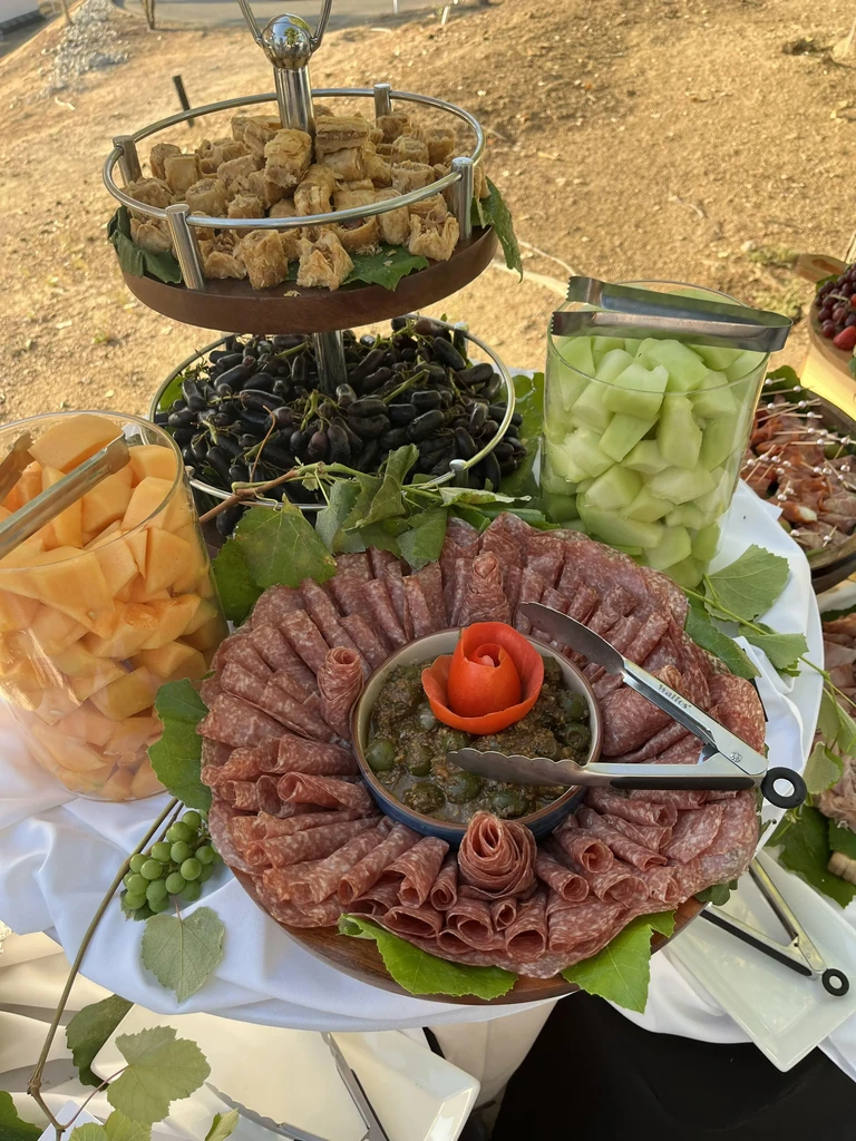 Outdoor buffet with charcuterie, fried items, grapes, and melon.