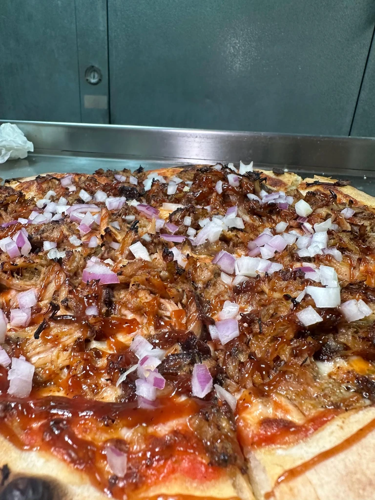 Close-up BBQ pizza, shredded meat, sauce, onions, separated slice.