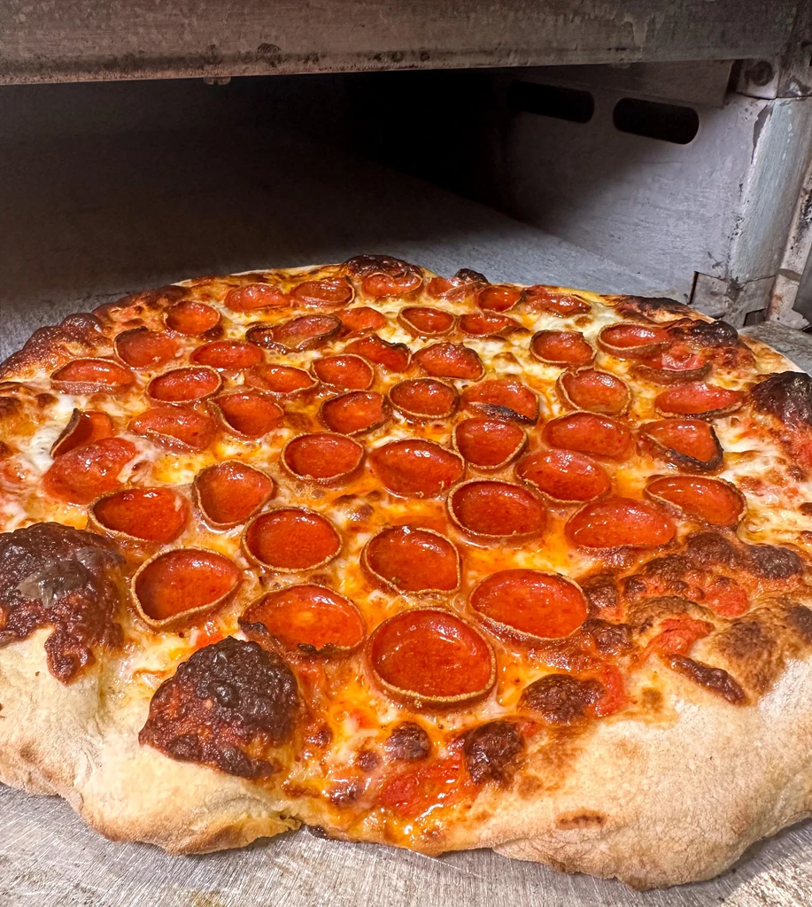 Freshly baked pepperoni pizza with bubbly cheese, commercial oven in background.