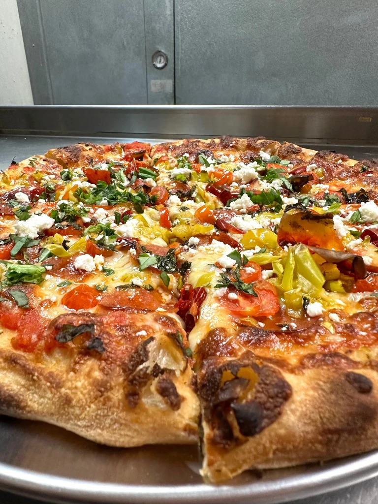 Freshly baked, sliced pizza with tomatoes, white cheese, herbs, and peppers.