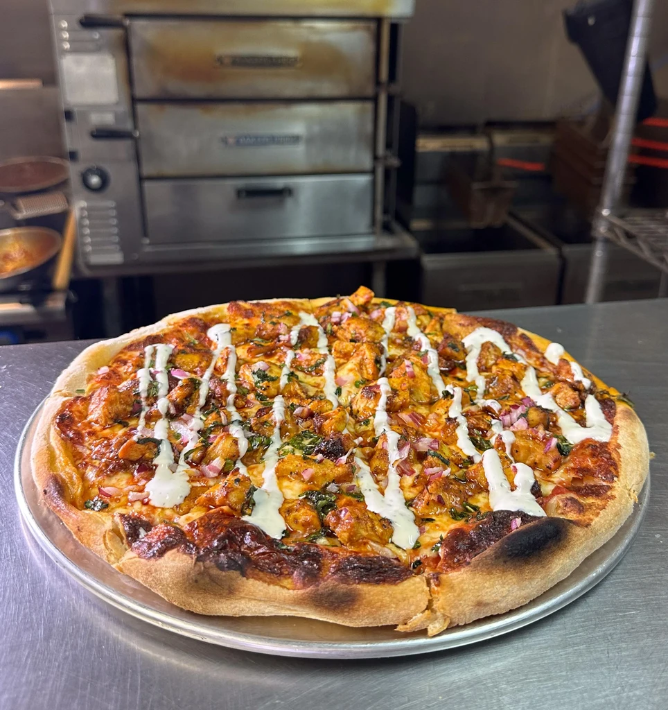 Well-baked chicken pizza, red onions, herbs, white sauce, professional kitchen.