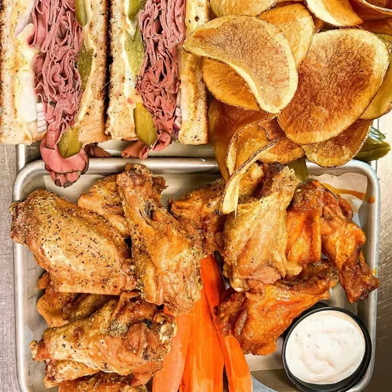 Metal tray: roast beef sandwich, chips, chicken wings, and carrots.