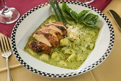 Seared chicken, gnocchi, green sauce in checkerboard-rimmed bowl on table.