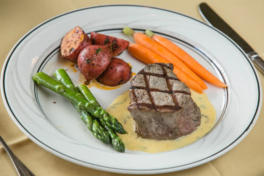 Grilled steak with creamy sauce, asparagus, potatoes, and carrots.