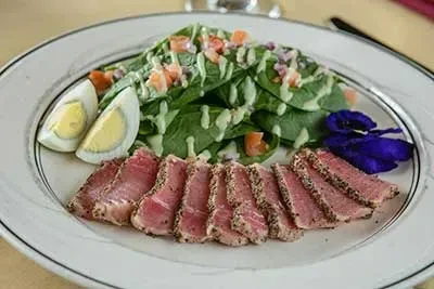 Plate of medium-rare seared tuna, egg, salad, purple flowers.