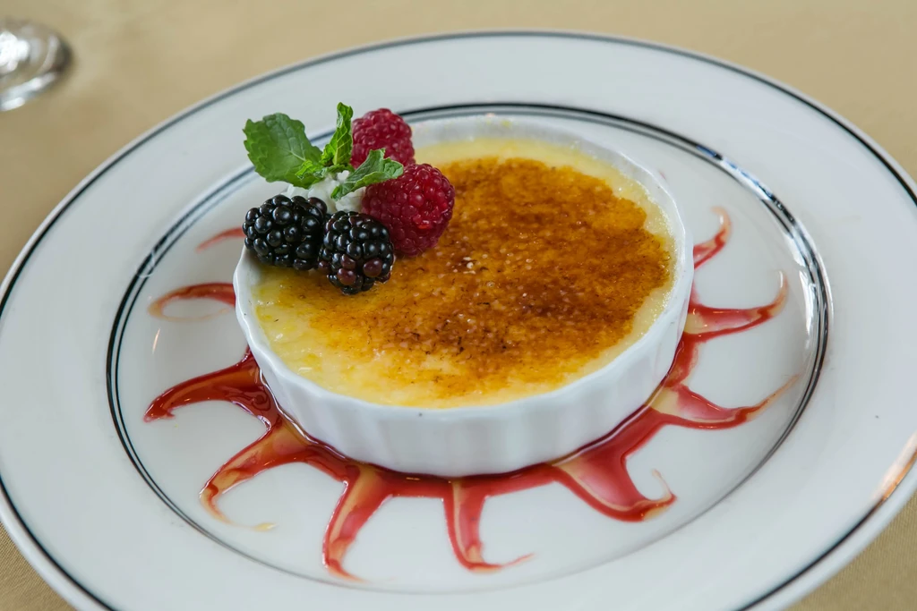 Crème brûlée with golden crust, fresh berries, mint, and berry sauce.