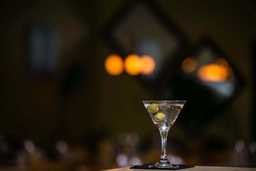 Martini glass with olives and condensation on a dark, blurred background.