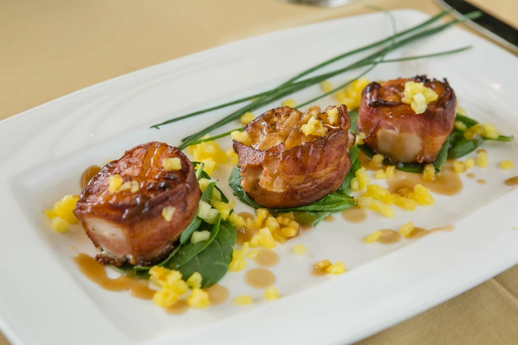 Three bacon-wrapped scallops with greens, fruit salsa, and brown sauce.
